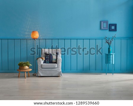 Blue wall and background room, decorative sofa and middle table, armchair and pillow detail, lamp and frame decoration with carpet decor.