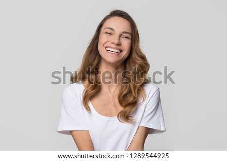 Happy cheerful young woman with beautiful face, teeth and hair laughing looking at camera on white light background, smiling pretty girl model having fun isolated on blank grey studio wall, portrait Royalty-Free Stock Photo #1289544925