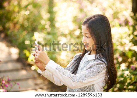 beautiful little asian girl with long hair taking a selfie against flower background using cellphone