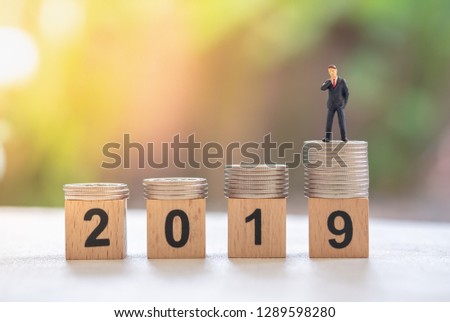 2019 New year, Business planning and saving concept. Close up of businessman miniature figure standing on stack of silver coins on number wooden block.