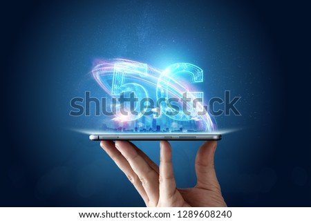 Creative background, male hand holding a phone with a 5G hologram on the background of the city. The concept of 5G network, high-speed mobile Internet, new generation networks. Mixed media. Royalty-Free Stock Photo #1289608240