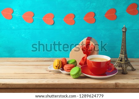 Valentine's day concept with coffee cup, macaroons, gift box and Eiffel tower on wooden table over heart shape garland background