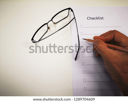 Businessmen use a pencil to make a checklist in a piece of paper and have glasses placed on a white table.