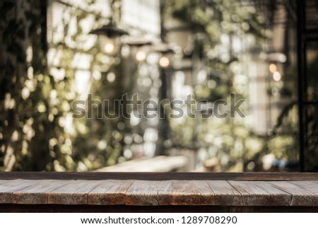 Wooden table in front of indoor garden with table and light bulb decorated with leaves and flowers in a garden, can used for display or montage your products.
