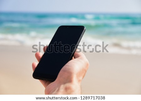 Mobile phone in male hand on the background of the beach and ocean. A young man makes a photograph of the ocean. Close-up. Sri Lanka.