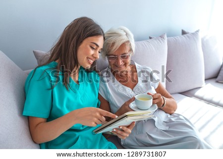 Happy patient is holding caregiver for a hand while spending time together. Elderly woman in nursing home and nurse. Aged elegant woman and tea time at nursing home 