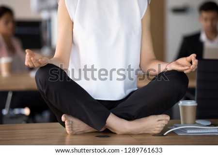 Close up view of woman sitting at work desk in lotus position doing exercises for relaxation or concentration at workplace, office meditation and yoga at work for no stress free relief concept