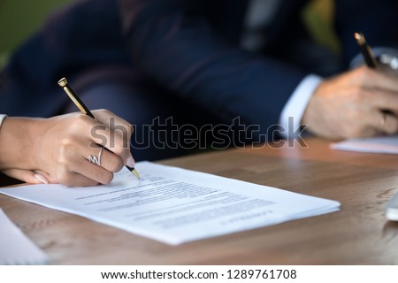 Close up view of woman and man signing document concluding contract concept making prenuptial agreement visiting lawyer office, female and male partners or spouses writing signature on decree paper Royalty-Free Stock Photo #1289761708