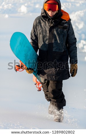 full length photo. man is going to snowboard on a rocky mountain