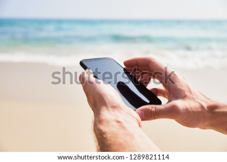 Mobile phone in male hand on the background of the beach and ocean. A young man makes a photograph of the ocean. Close-up. Sri Lanka.