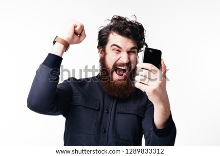 Handsomen bearded young man is  celebrating his wonn and gesturing over white background