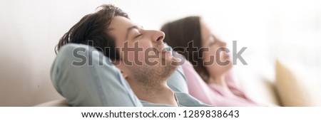 Spouses with closed eyes breathing fresh air dreaming resting on couch put hands behind heads, close up focus on man. Leisure and relaxation concept. Horizontal photo banner for website header design Royalty-Free Stock Photo #1289838643
