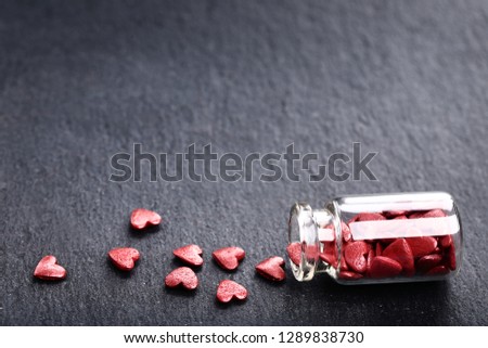 Red heart shaped sprinkles in glass bottle on black background