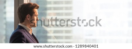 Panoramic image businessman in suit looks through office window at big city modern building architecture dream about future. Horizontal photo banner for website header design with copy space for text
