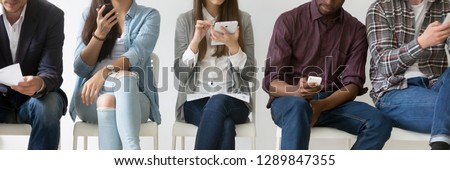 Horizontal photo multiracial young people sitting in row use electronic devices vacancy candidates wait in queue, ignore each other holding phones addicted by gadgets, banner for website header design