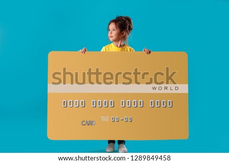 little cute girl holding big gold credit bank card isolated on blue background
