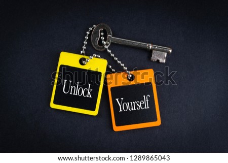 UNLOCK YOURSELF inscription written on wooden tag and key on black background with selective focus and crop fragment. Business and education concept