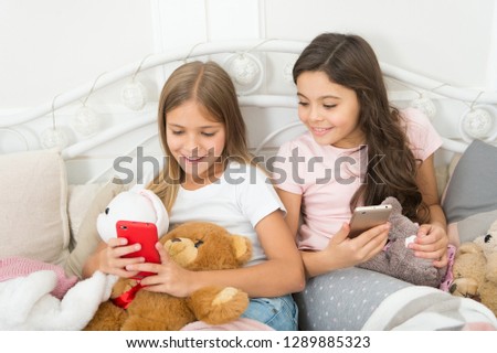 Sharing great pictures. Merry Christmas and Happy New Year greetings. Little girls use smartphone in bed. Happy little children with mobile phone. Ordering gifts for Christmas and New Year by phone.