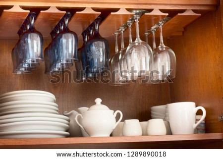 White dinnerware and blue and clear wine glasses neatly organized inside a wooden cupboard Royalty-Free Stock Photo #1289890018