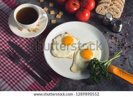 American/English/European traditional morning breakfast with sunny side up fried eggs on pan, tea, bread, cookies, vegetables and green.