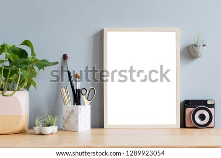 Stylish home interior with mock up photo frame on the brown wooden table with office accesories, instant camera, tillandsia in design pots, plant in stylish pot. Grey walls. Minimal concept of mockup.
