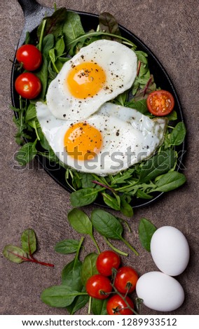 Fried eggs with fresh herbs and cherry tomatoes at pan for breakfast, on brown background. Concept of tasty and healthy lifestyle