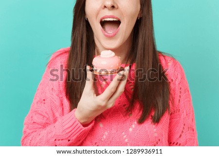 Cropped image of young girl in knitted pink sweater hold in hand eating cake isolated on blue turquoise wall background studio portrait. People sincere emotions, lifestyle concept. Mock up copy space