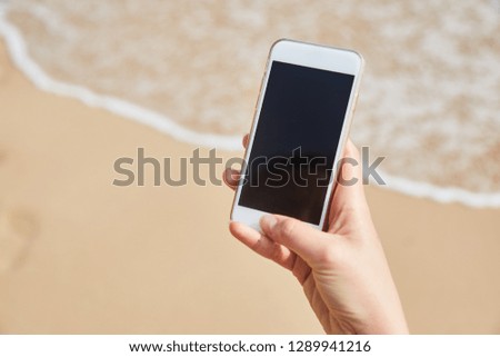 Mobile phone in female hand on the background of the beach and ocean. A young girl makes a photograph of the ocean. Close-up. Sri Lanka.