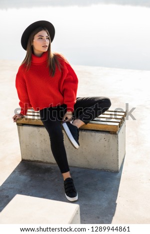 Beautiful woman in black hat sitting on a bench in a city park