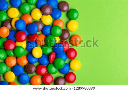 Glazed colored chocolate candies are gathered on bright green background. Top view. Copy space