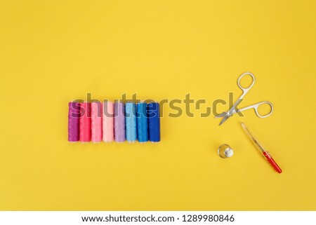 Colorful yellow thread spools with seam accessories over bright yellow background, above view