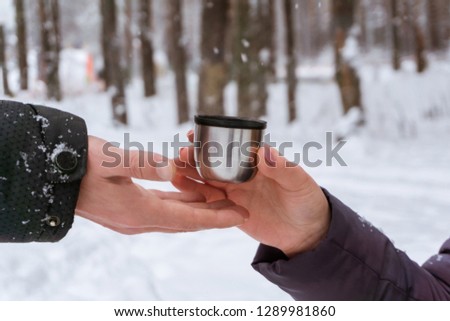 female hand in a winter park passes a mug with a hot drink to friend