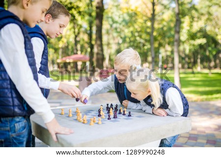 The topic children learning, logical development, mind and math, miscalculation moves advance. large family brothers and sister Caucasian boys and girl playing chess park bright sunny weather autumn.