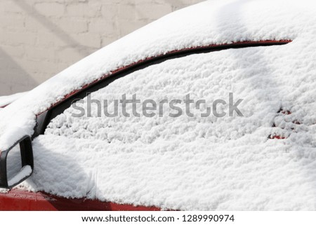 Close up of frozen red car covering with snow at winter day, side window on snowy background. Texture of snow and snowflakes for the New Year, winter holidays. Outdoors, nature concept