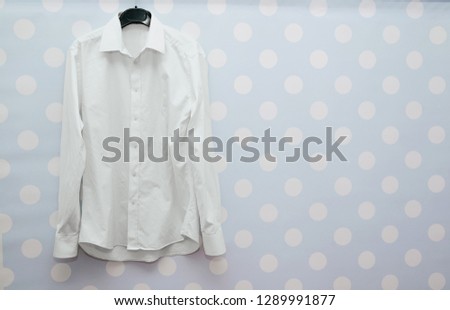 A white business shirt sloppily hanged on a hanger. Shirt thrown on a blue pastel wall. Using crumpled clothes to work, a problem with ironing clothes.