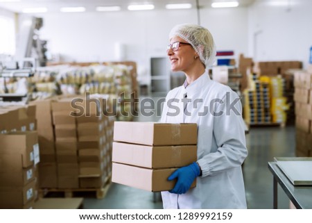 Happy Caucasian female worker holding boxes while standing in warehouse.
