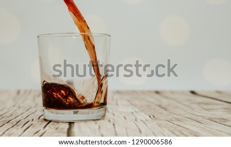 Pouring cola into a glass. The cola flows into the glass on the wooden floor. Brown liquid is poured into a glass. The concept of drinking and gaining strength, thirst.