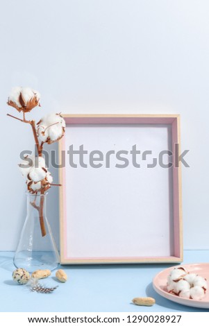 Mock up white frame and dry cotton twigs in vase on book shelf or desk. White-blue colors. Minimalistic concept.