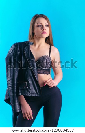 beautiful girl with long hair in a black leather jacket on one shoulder and pants looking at the camera on a blue background
