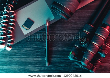 Top view of a desk working with laptop keyboard, modern camera, tripod and a black pen on a wood background. Freelance, creative or online education concept. Red and blue light