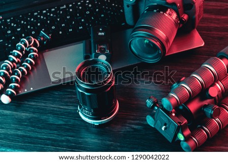 A workspace with laptop, modern camera, lens, tripod and a black pen on a wood background. Freelance or creative man or woman. Red and blue light