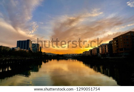 Dramatic Waterfront City Sunset with River and Colorful Clouds in Sky with Silhouetted Buildings