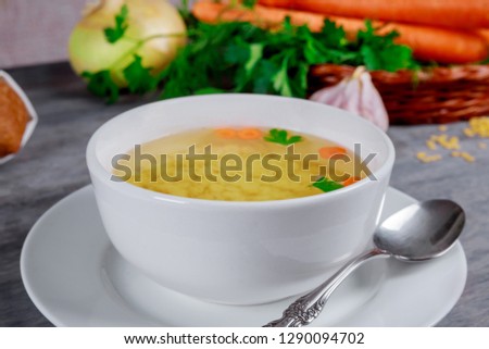 Homemade chicken bouillon or broth in a bowl over vegetable background, view from above