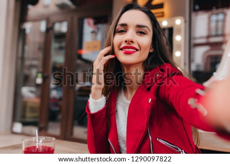 Ecstatic white female model making selfie in good day. Outdoor portrait of cute brunette lady wears elegant red jacket.