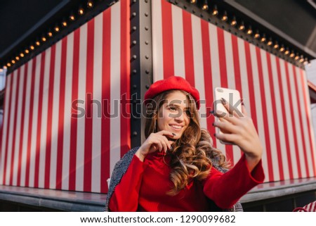 Good-looking brunette girl with happy face expression making selfie on striped background. Photo of spectacular white female model in sweater taking picture of herself.