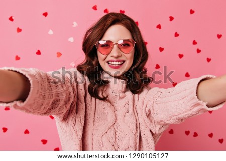 Pretty ginger girl smiling on pink background. Studio shot of caucasian lady making selfie in valentine's day.