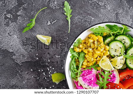 Vegan buddha bowl. Bowl with fresh raw vegetables - cucumber, tomato, watermelon radish, lettuce, arugula and corn. Fresh salad. Vegetarian food. Top view. Flat lay