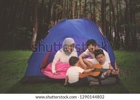 Picture of young Muslim family playing a guitar while camping in the forest 