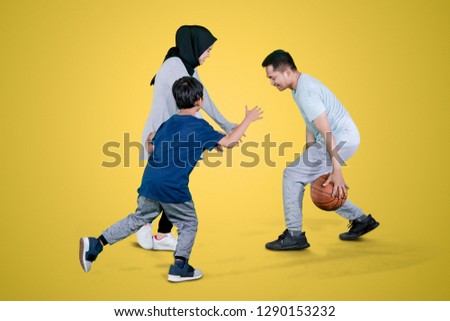 Picture of Muslim family playing basketball in the studio while exercising together with yellow background
