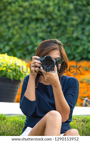 Hand woman holding the camera Taking pictures Background of trees and flowers